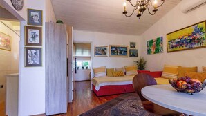 A compact living space with a bed, a dining table with a fruit bowl, and various framed pictures on the walls. - Holiday apartment with large terrace (Jadranovo)