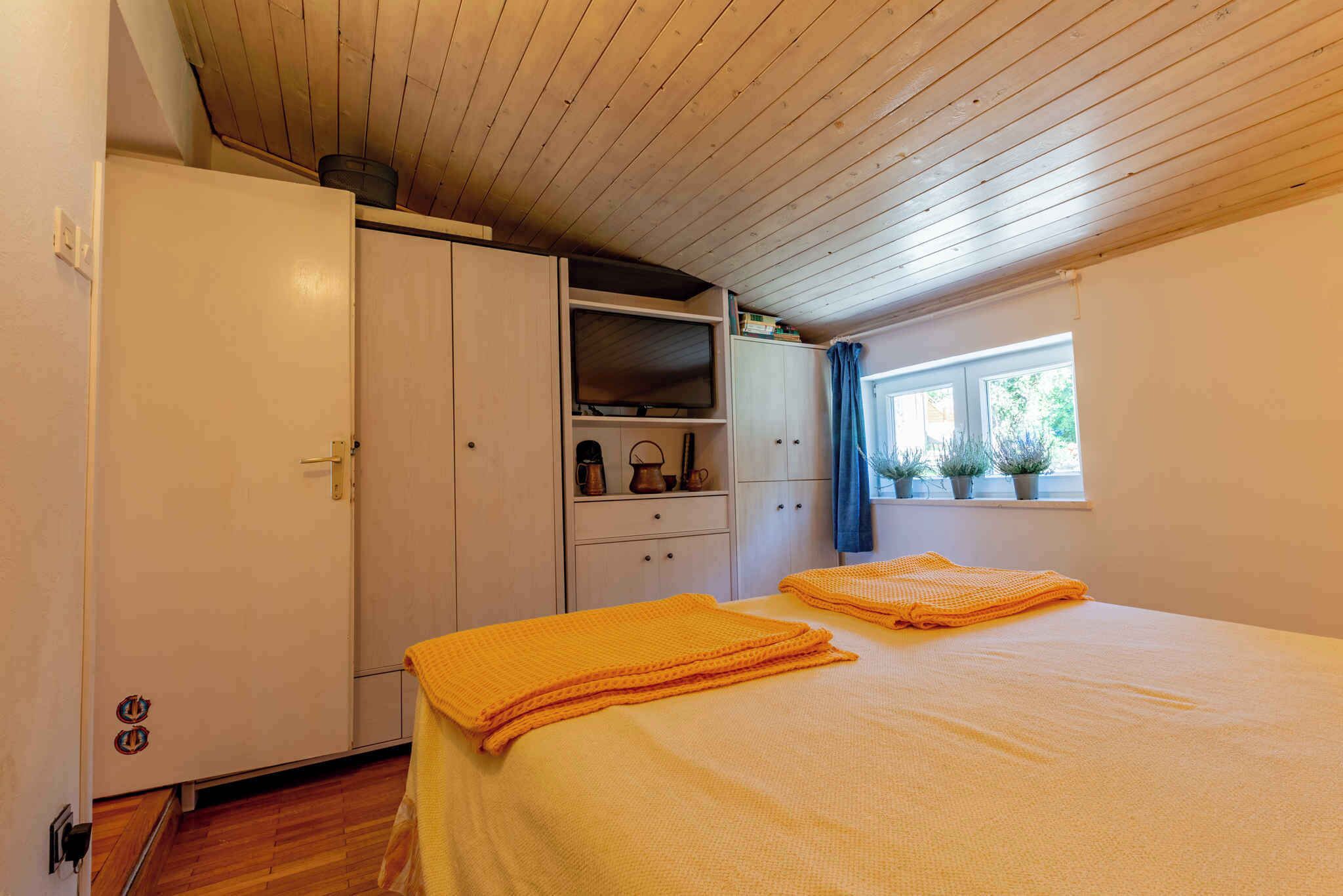 A bedroom with a bed, a wardrobe, a shelf with items, and a window with plants.