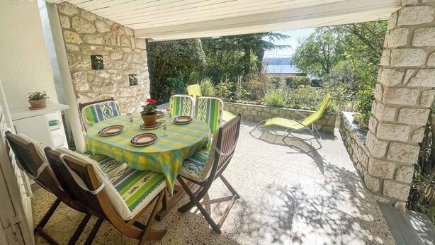 An outdoor patio with a table set for dining, surrounded by stone walls and chairs, overlooking a scenic view. - Holiday apartment with large terrace (Jadranovo)