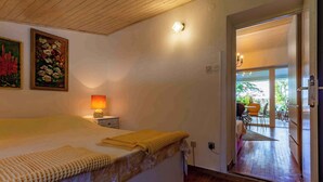 A bedroom with a bed, a nightstand, a lamp, and a painting on the wall. There is a door leading to a balcony with outdoor furniture. - Holiday apartment with large terrace (Jadranovo)
