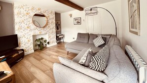 A modern living room with a grey sofa, wooden flooring, a TV, and a fireplace. - Capella Cottage, 2 Bedroom, Sleeps 4 (Lincoln)