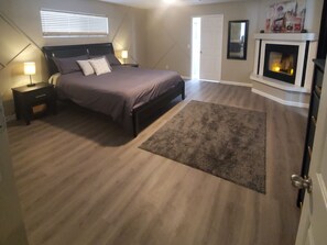 Une chambre à coucher avec un lit, des tables de chevet, un tapis, une cheminée et une porte.