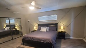 Un dormitorio con cama, mesitas de noche, ventilador de techo y un espejo grande.