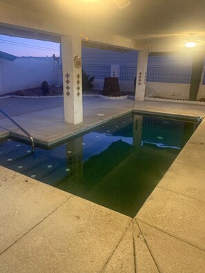 Una piscina interior con agua cristalina, rodeada de paredes de azulejos y pilares de hormigón.
