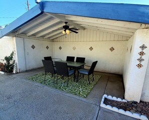 Une terrasse couverte avec une table et des chaises, un ventilateur de plafond et des carreaux décoratifs sur les murs.