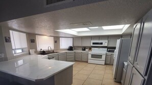 Una cocina moderna con una isla grande, electrodomésticos blancos y un tragaluz.