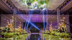 A stage with a reflective floor, surrounded by floral arrangements and candles, under a draped ceiling with hanging decorations. - Empark Grand Hotel (Guiyang)