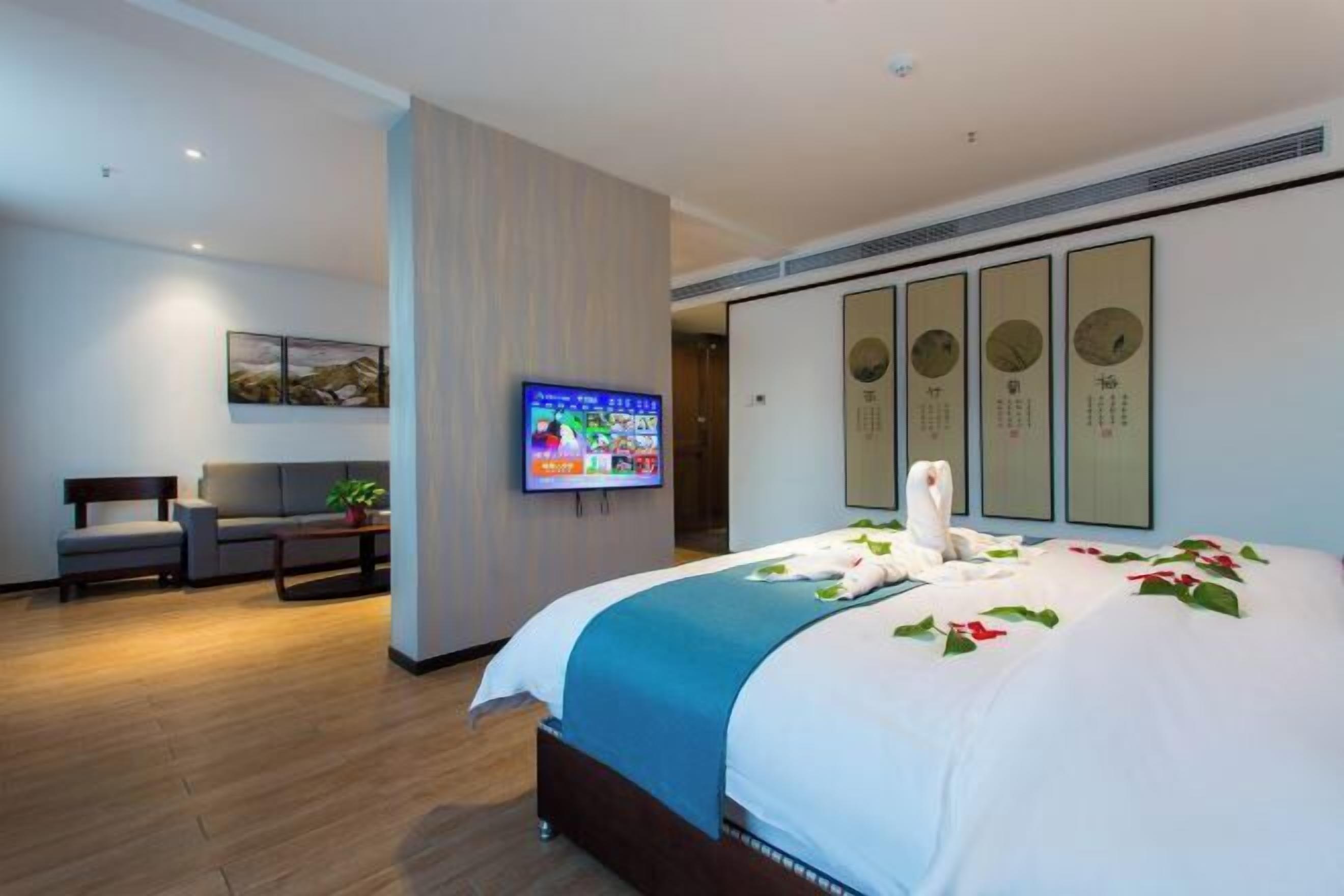 Habitación de hotel con cama, televisor, sofá y un muro decorado con obras enmarcadas.
