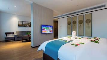 Habitación de hotel con cama, televisor, sofá y un muro decorado con obras enmarcadas.