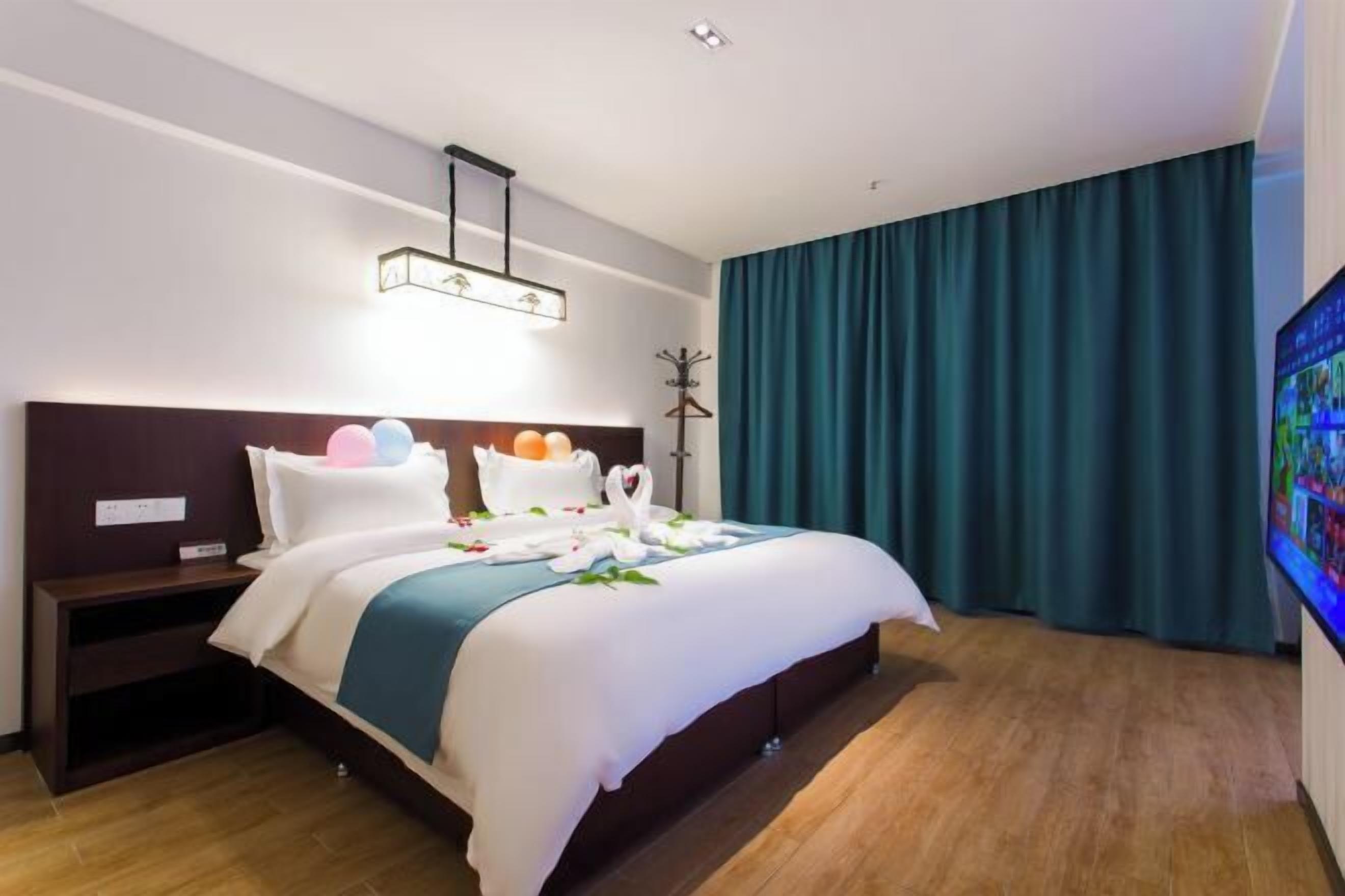 A hotel room with a neatly made bed, a bedside table, a wall-mounted TV, and a large window with curtains.