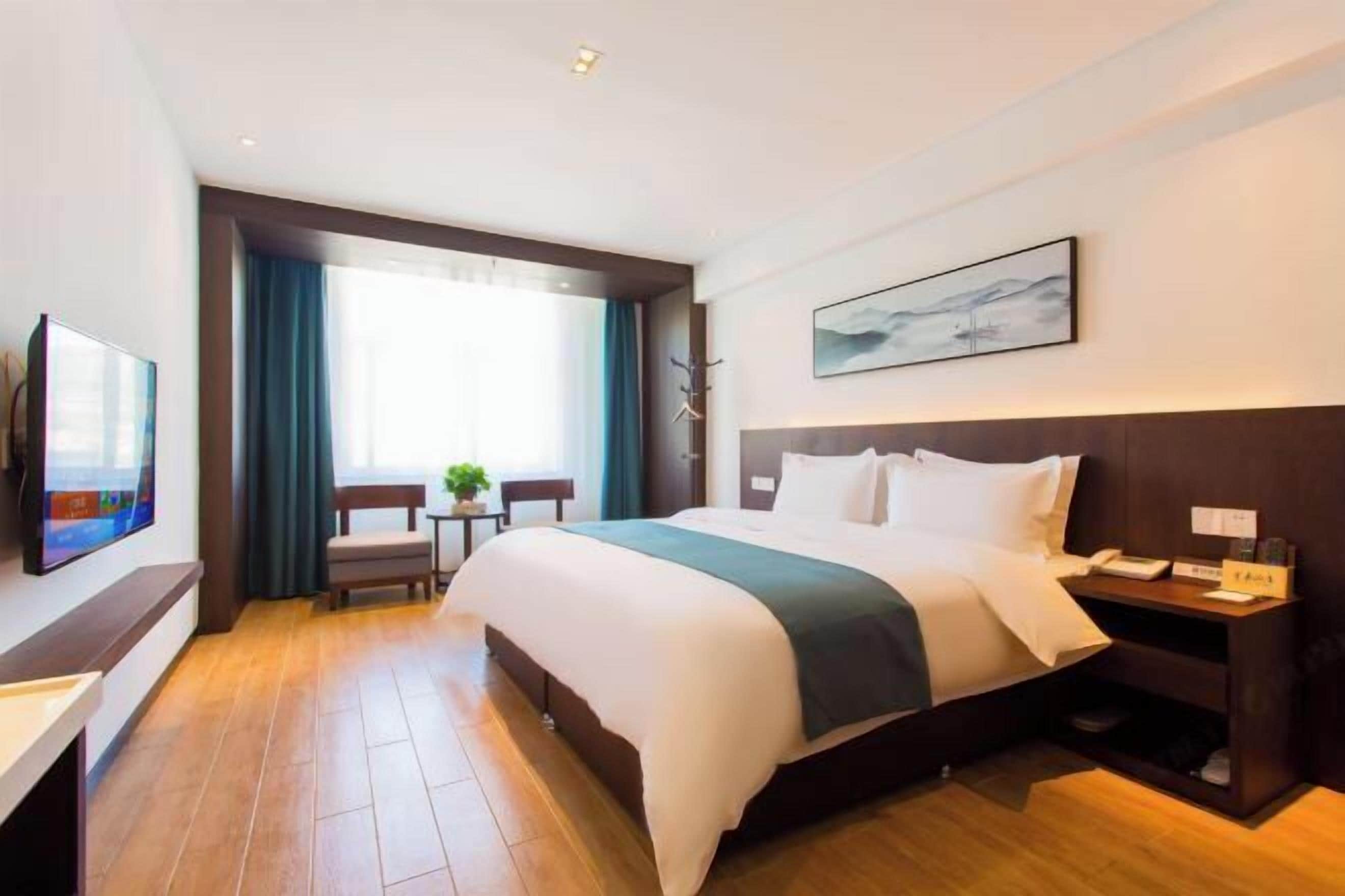 Una habitación de hotel con cama, escritorio, televisor, ventana con cortinas y un cuadro en la pared.