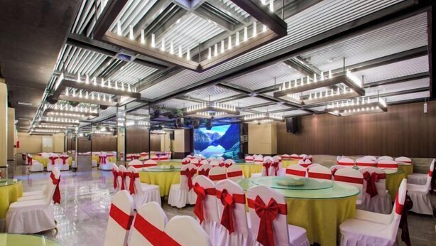 A banquet hall with round tables and chairs, each with a white cover and red sashes. - Jinyue Hotel (Yan'an)