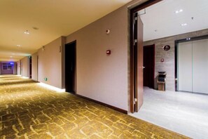 Un pasillo de hotel con alfombra estampada, una puerta de madera y una zona de recepción con mostrador y armarios.
