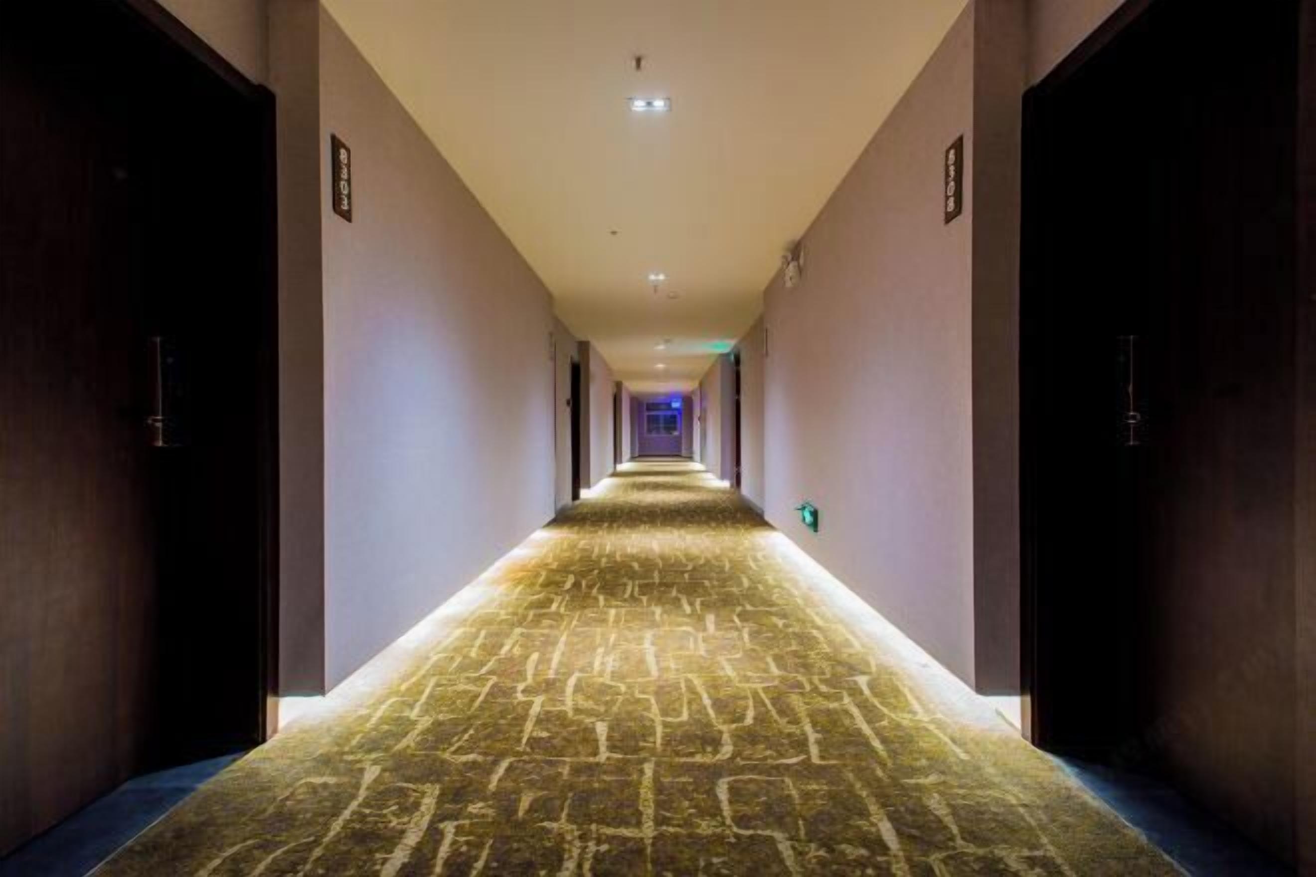 A hotel hallway with a carpeted floor, doors on both sides, and a light at the end.