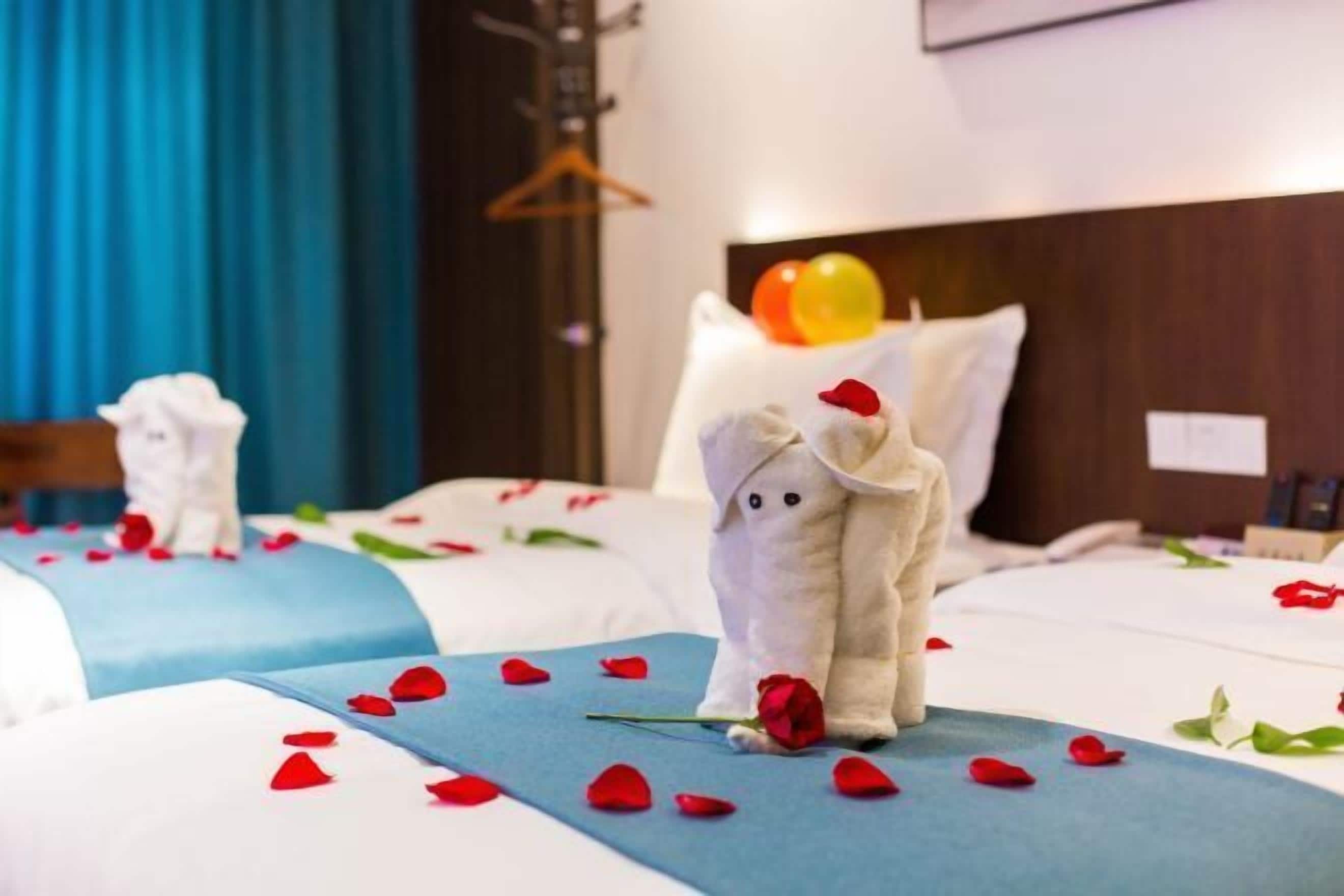 Une chambre d’hôtel avec deux lits, chacun décoré de pétales de rose et surmonté d’un ours en peluche tenant une rose.