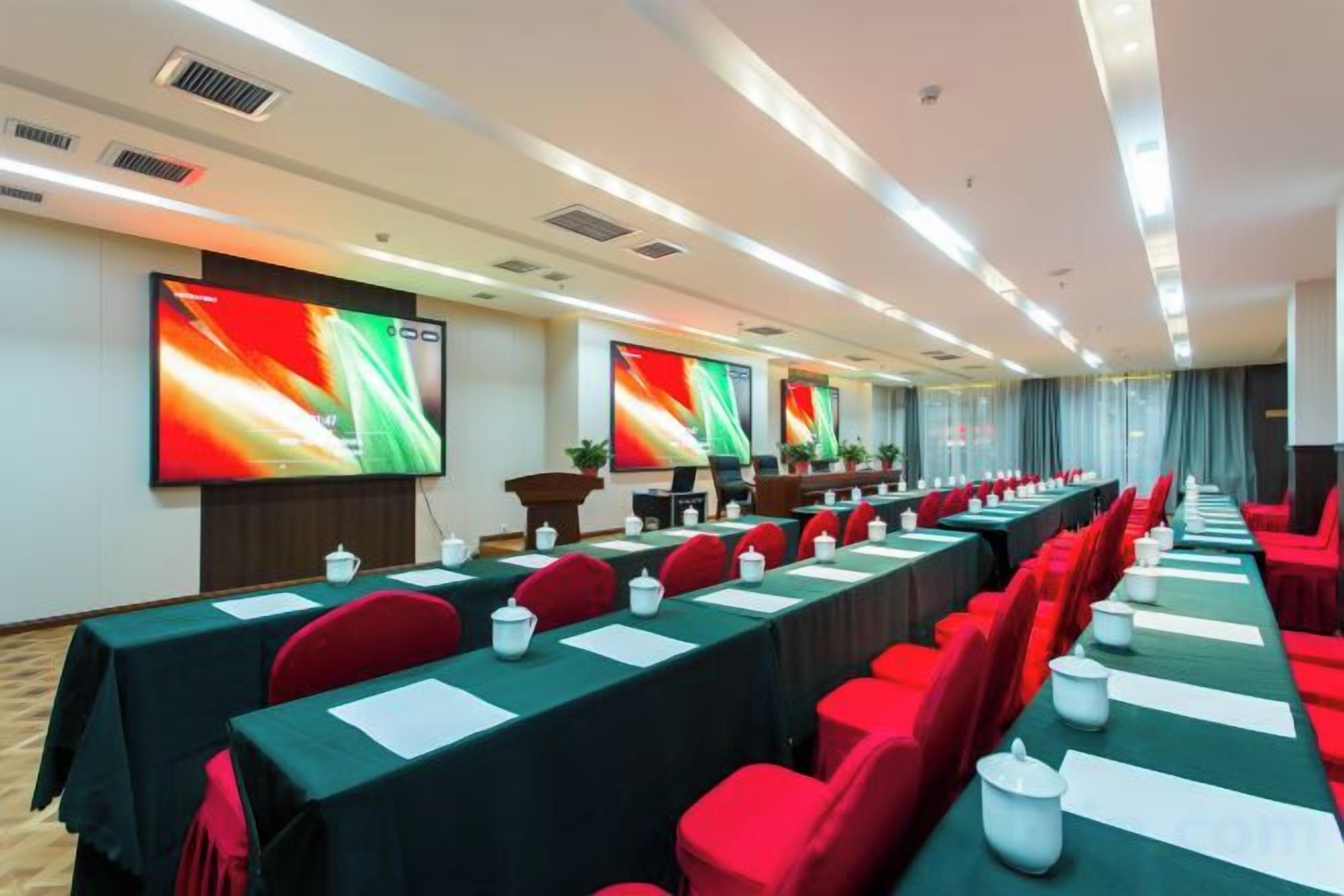 A conference room with long tables, red chairs, and large screens on the walls.