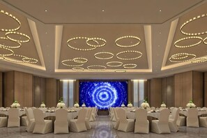 Une salle de banquet avec des tables rondes, une scène centrale et un plafond orné de luminaires circulaires.