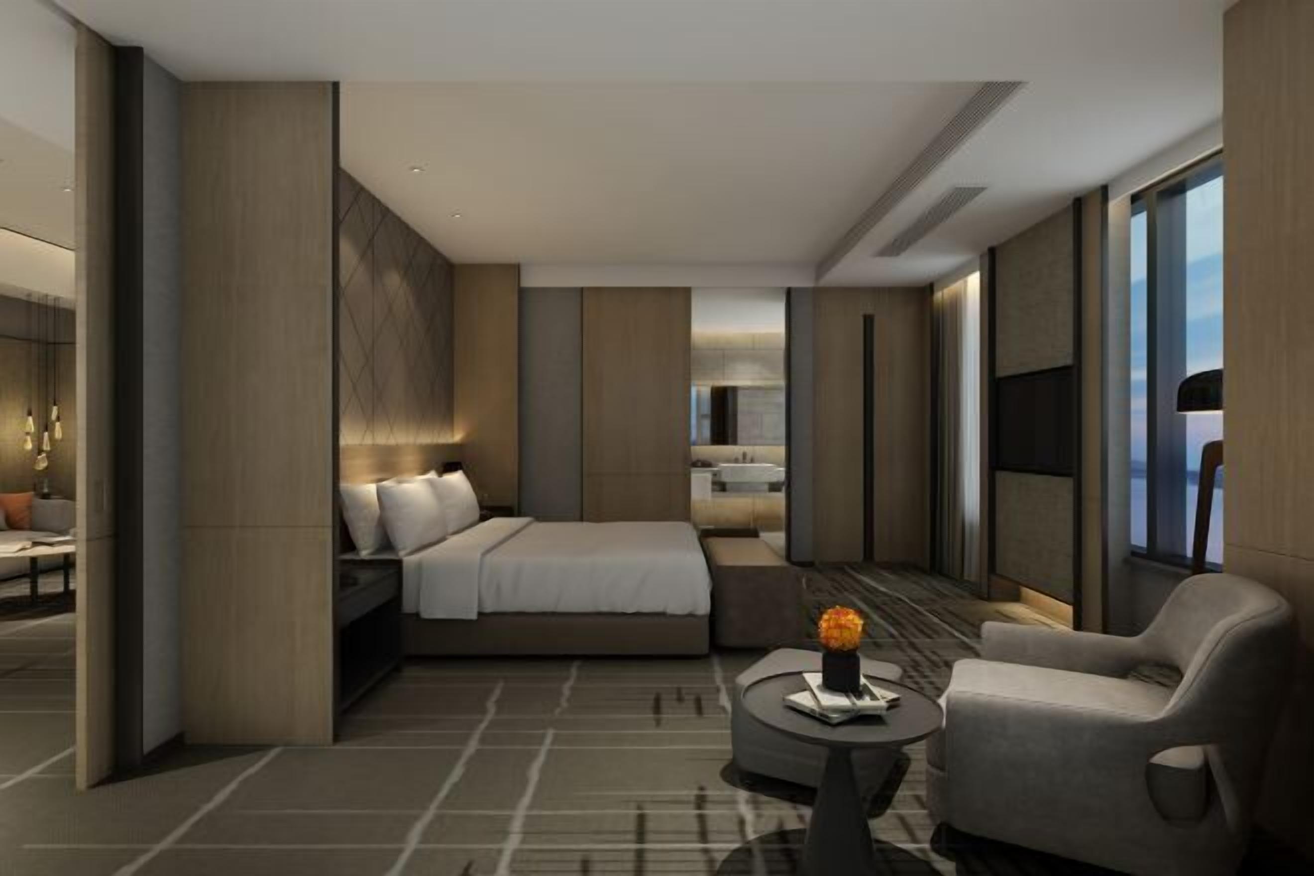 Une chambre d’hôtel moderne dotée d’un grand lit, d’un coin salon avec une table basse et offrant une vue sur la ville grâce à de grandes fenêtres.