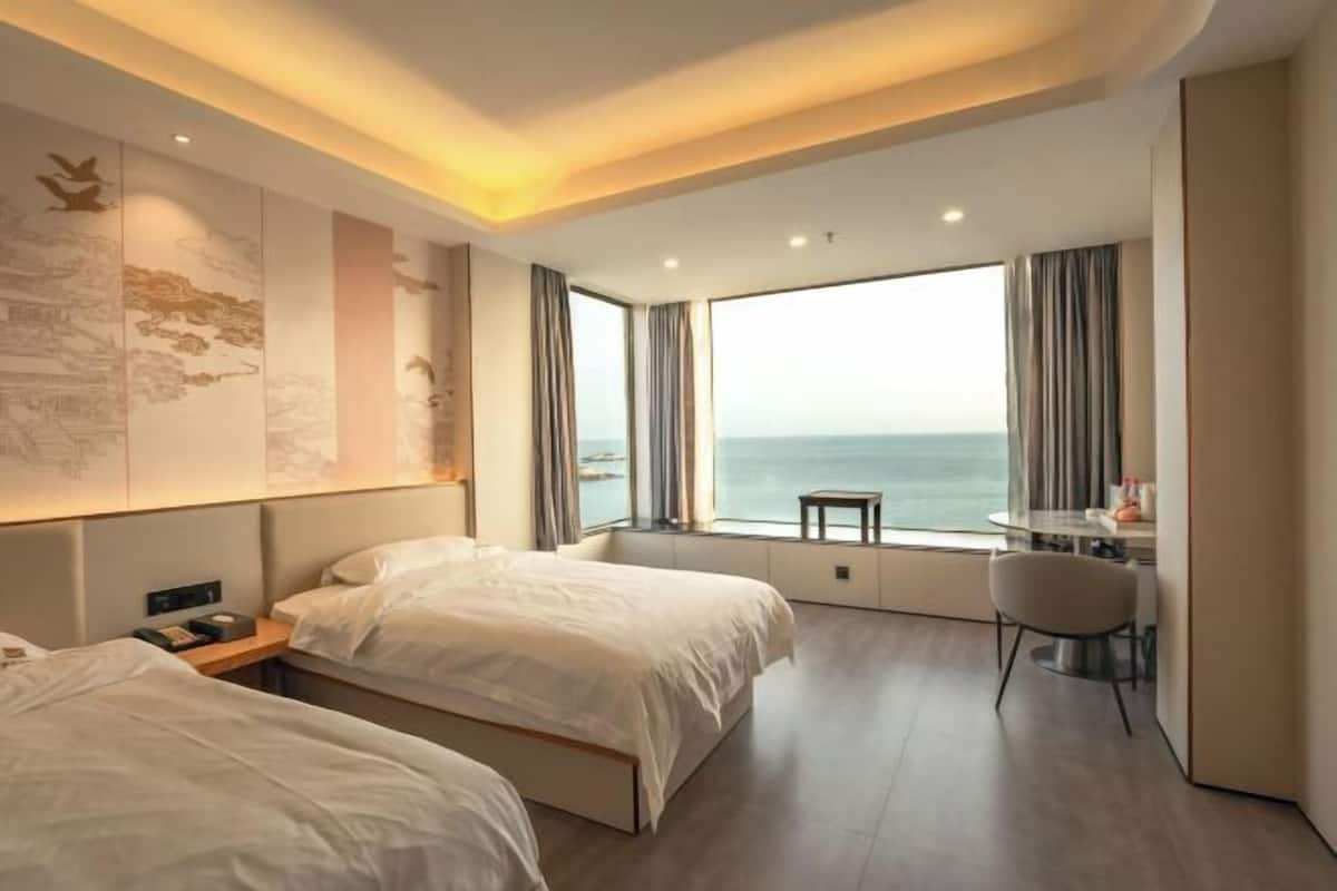 Une chambre d’hôtel avec deux lits, un bureau, une chaise et une grande fenêtre donnant sur la mer.