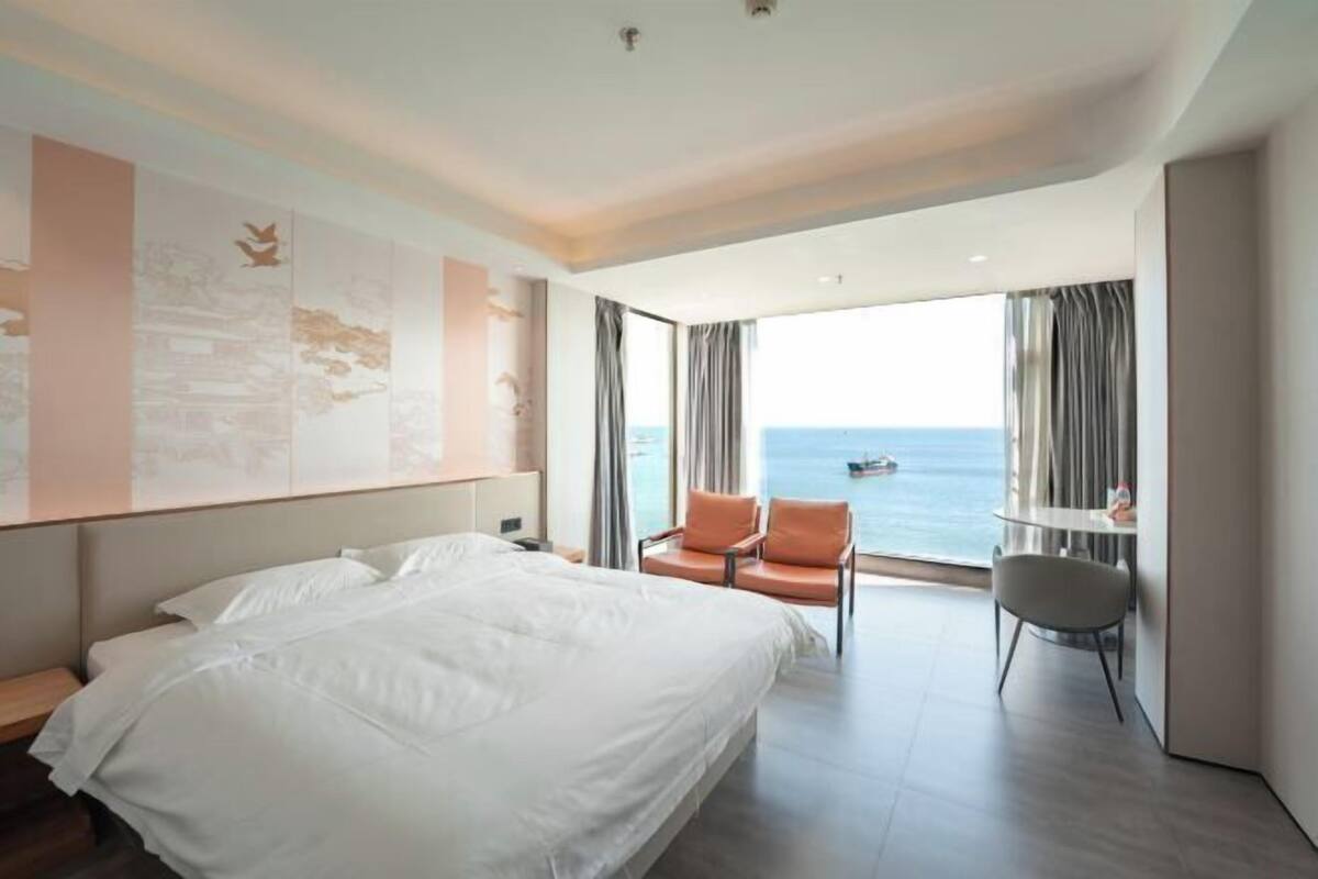 Une chambre d’hôtel dotée d’un grand lit, d’un coin salon avec vue sur la mer et d’un balcon.