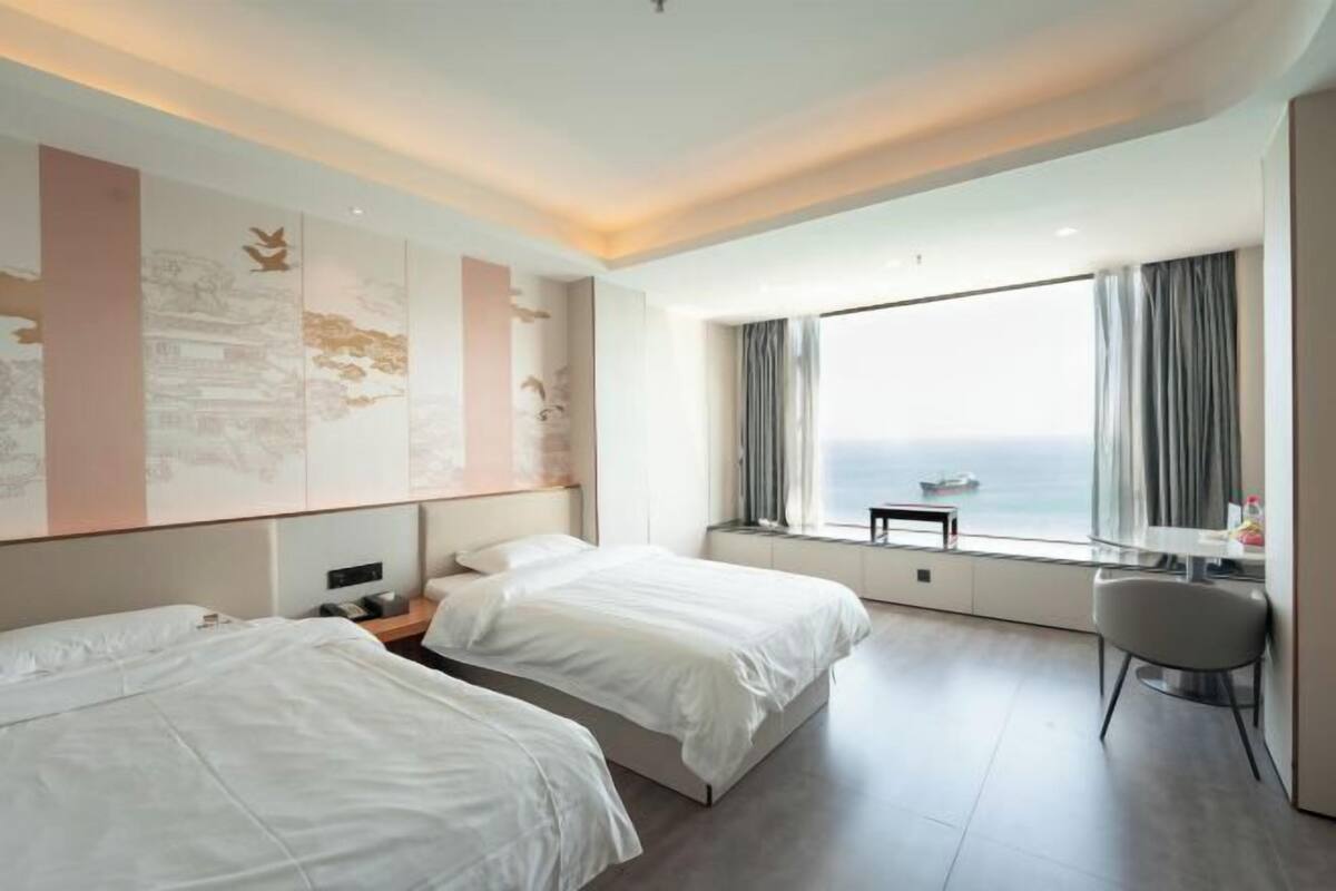 Une chambre d’hôtel avec deux lits, un bureau, une chaise et une grande fenêtre donnant sur un beau paysage.