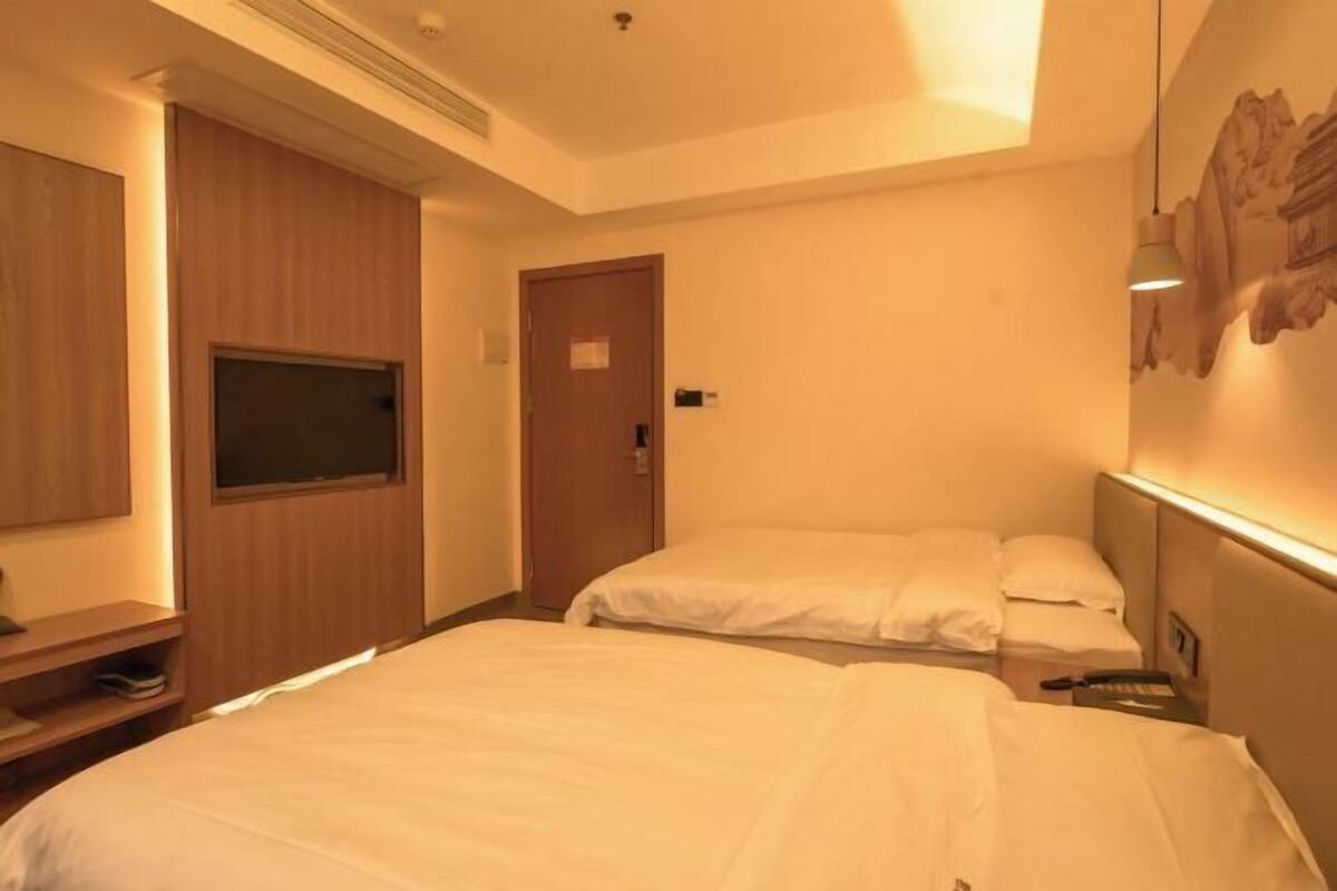 Une chambre d’hôtel avec deux lits, une télévision, une porte et une œuvre d’art accrochée au mur.