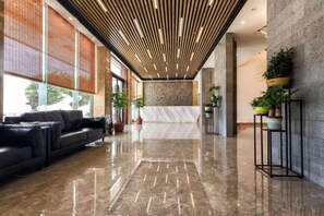 A lobby with a black leather sofa, a marble reception desk, and potted plants. - Junyue Prince Hotel (Shanwei)