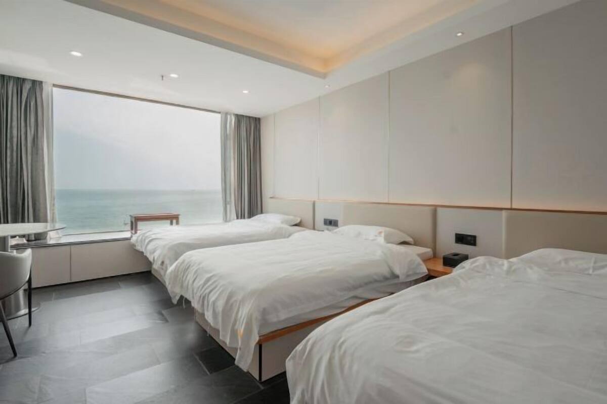 Une chambre d’hôtel avec trois lits, un bureau et une vue sur la mer.