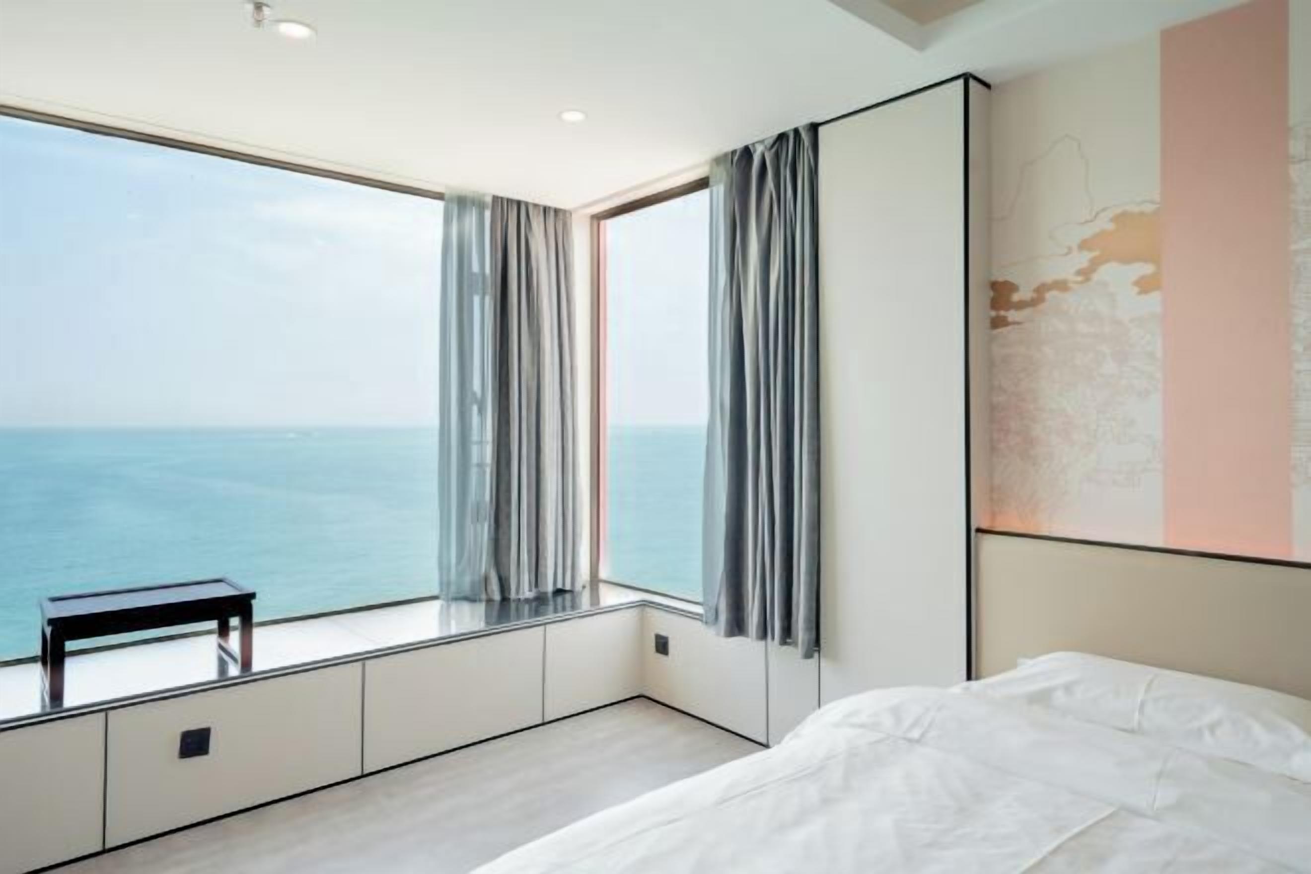 A bedroom with a large window, a bed, and a small table.