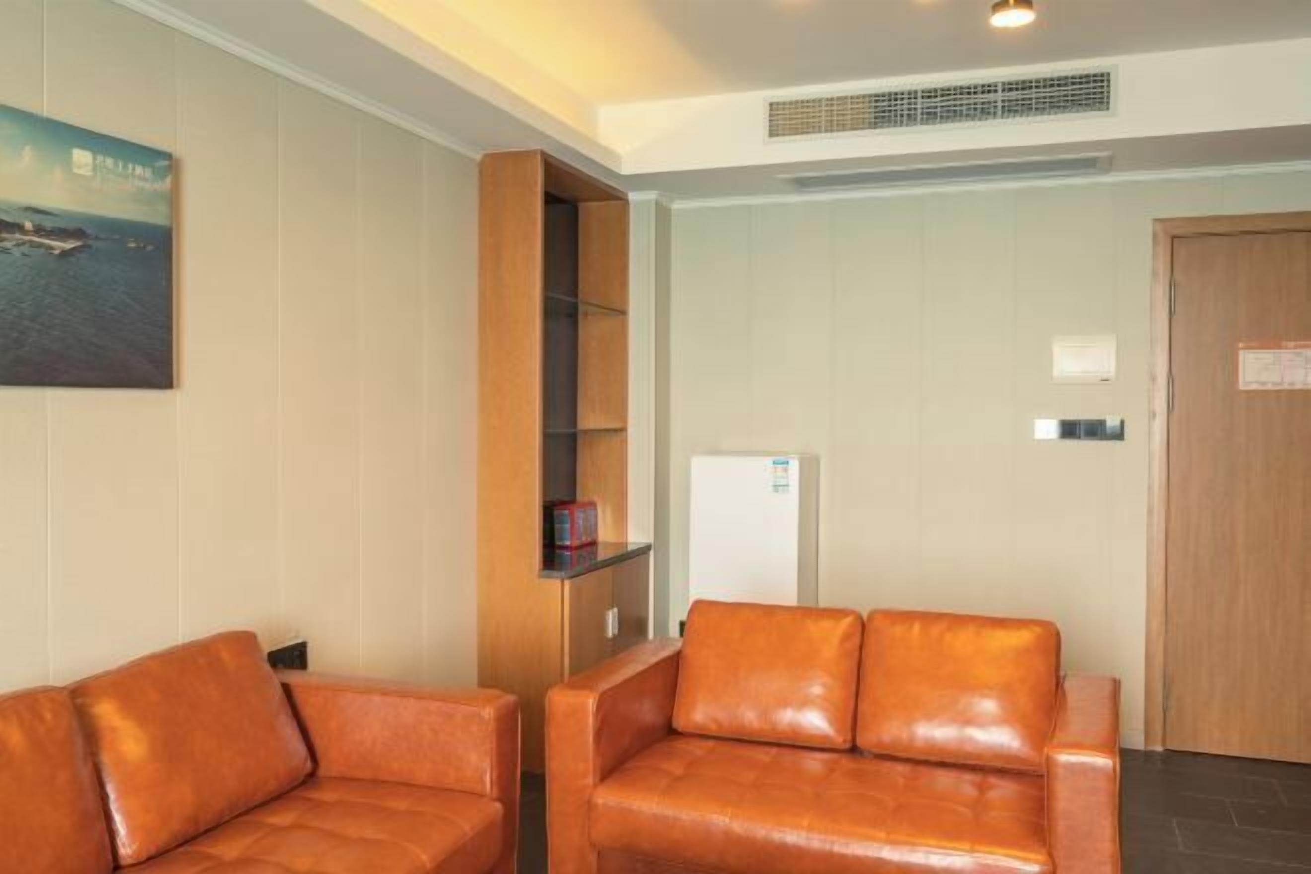 A room with a brown leather sofa, a wooden cabinet, a white door, and a wall-mounted picture.