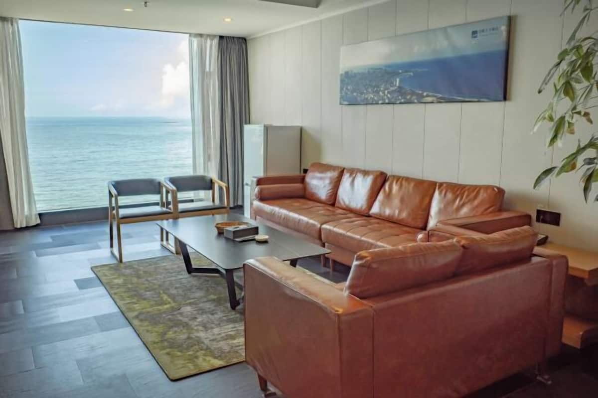 Un salon moderne avec un canapé en cuir, une table basse et une vue sur la mer grâce à de grandes fenêtres.