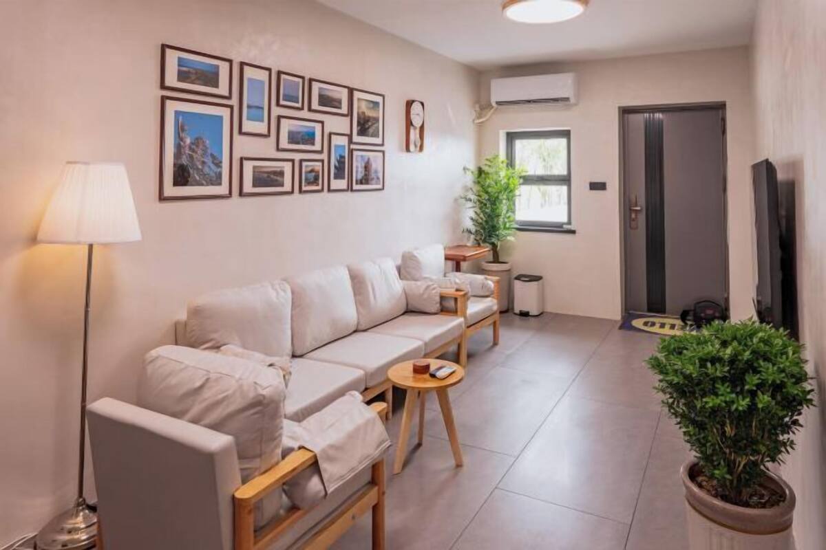 Un salon moderne comprenant un canapé, des fauteuils, une petite table, une lampe, des tableaux encadrés au mur, une plante en pot et un téléviseur.
