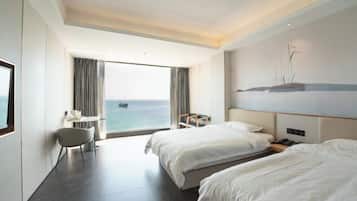 Habitación de hotel con dos camas, un escritorio, una silla y un ventanal con vistas al mar.