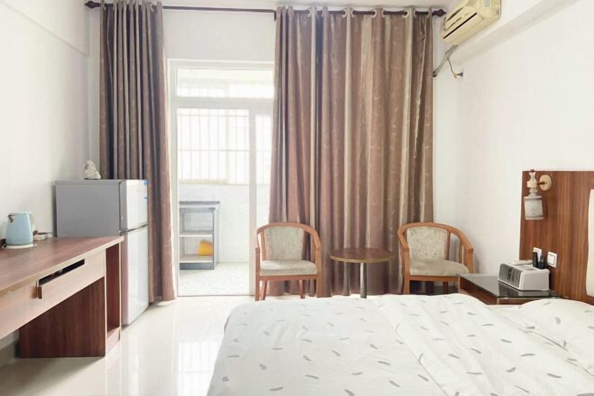 A hotel room with a bed, two chairs, a desk with a kettle, and a small table.