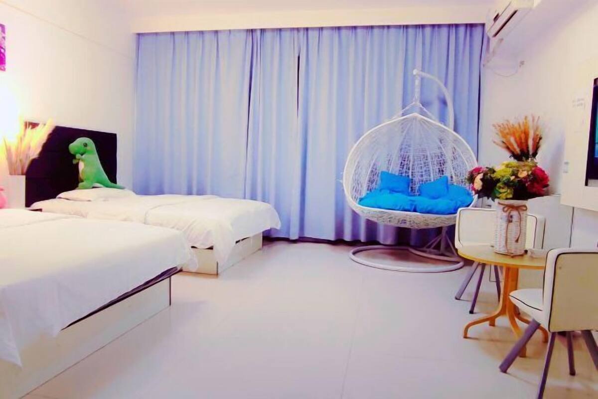 Une chambre d’hôtel avec deux lits, un fauteuil suspendu, une petite table avec un vase et un téléviseur fixé au mur.