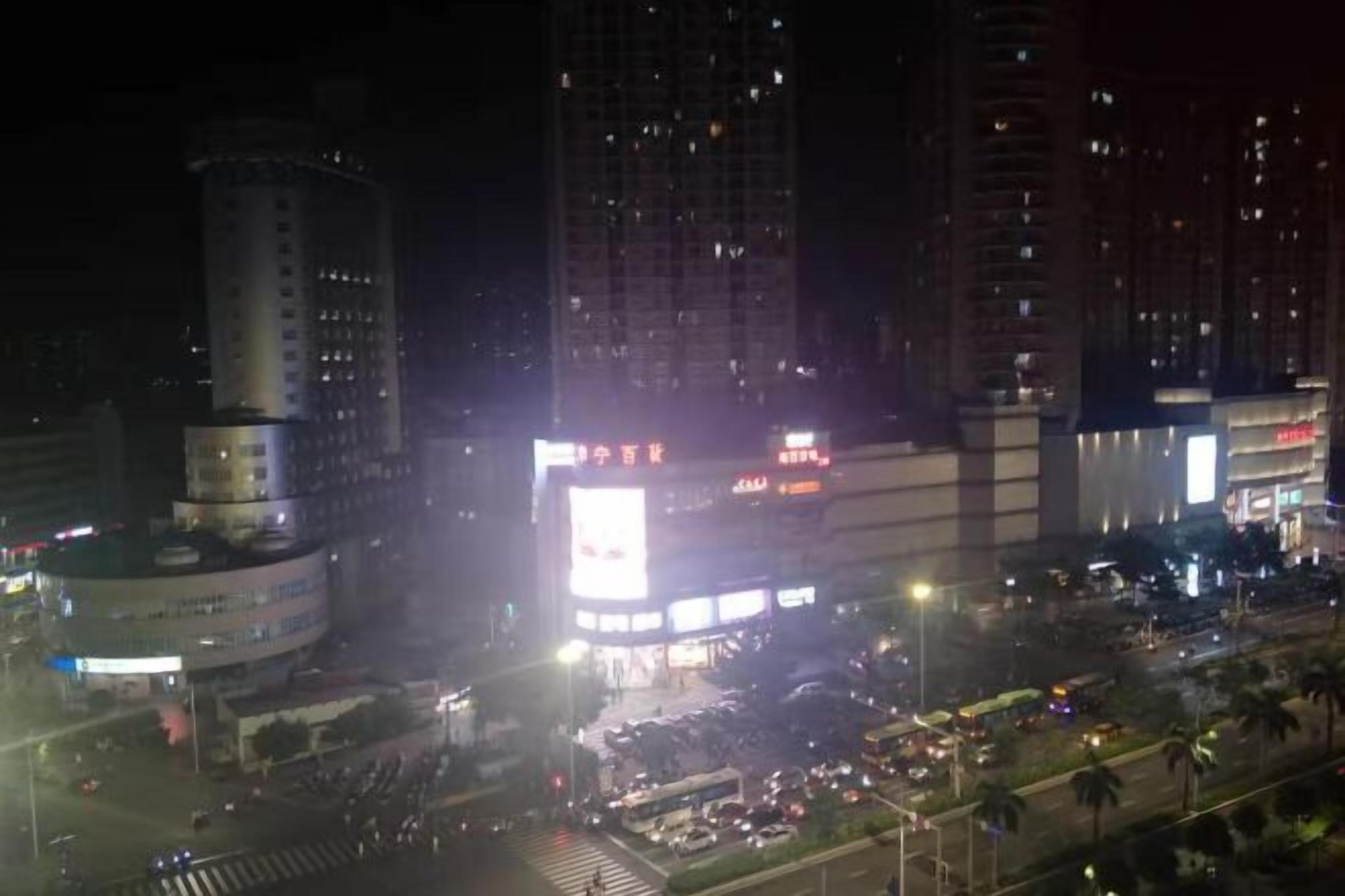 A nighttime cityscape with tall buildings, a busy intersection, and illuminated billboards.