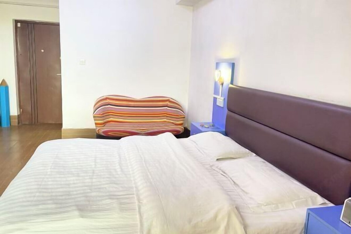 A bedroom with a large bed, a striped chair, a nightstand, and a wall-mounted lamp.