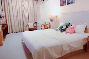 A neatly made bed with a white bedspread, a small wooden table with a chair, and a wall-mounted lamp.