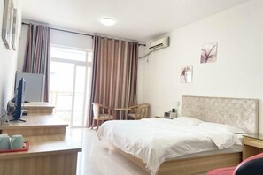 Ein Hotelzimmer mit Bett, Schreibtisch inklusive Computer, Stuhl und einem Fenster mit Vorhängen.