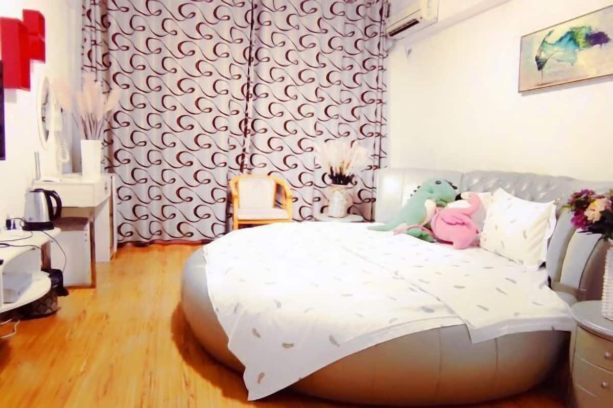 Une chambre à coucher avec un lit rond, une table de chevet, une chaise et un rideau orné d’un motif tourbillonnant.