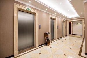 A hotel corridor with three elevators, a marble-tiled floor, and a modern design.