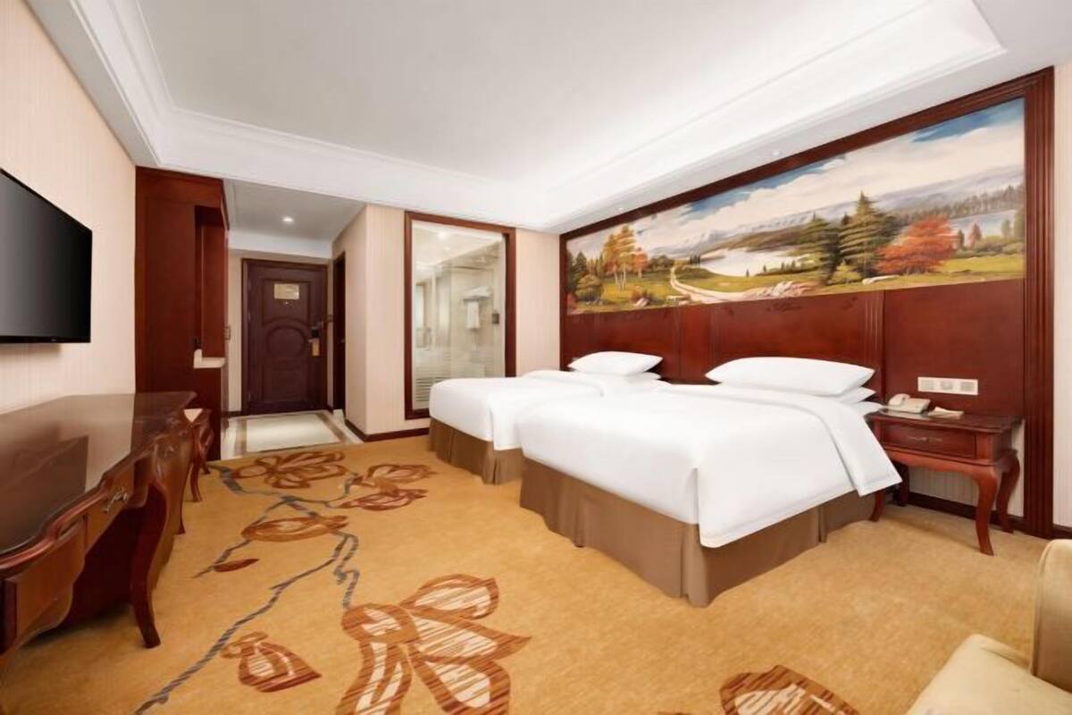 A hotel room with a bed, a desk, a TV, and a painting on the wall.