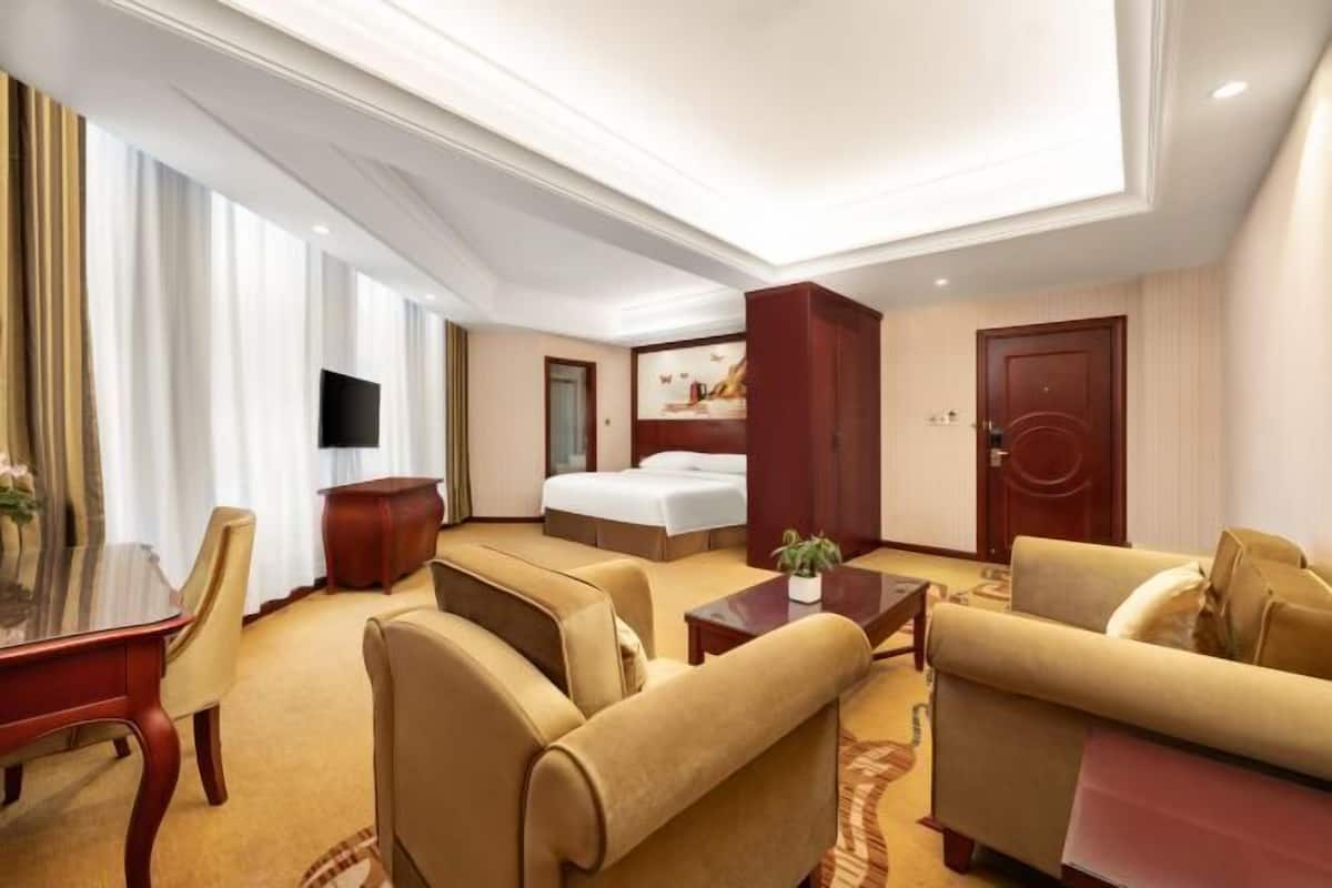 A hotel room with a bed, sofa, armchair, TV, and a desk.