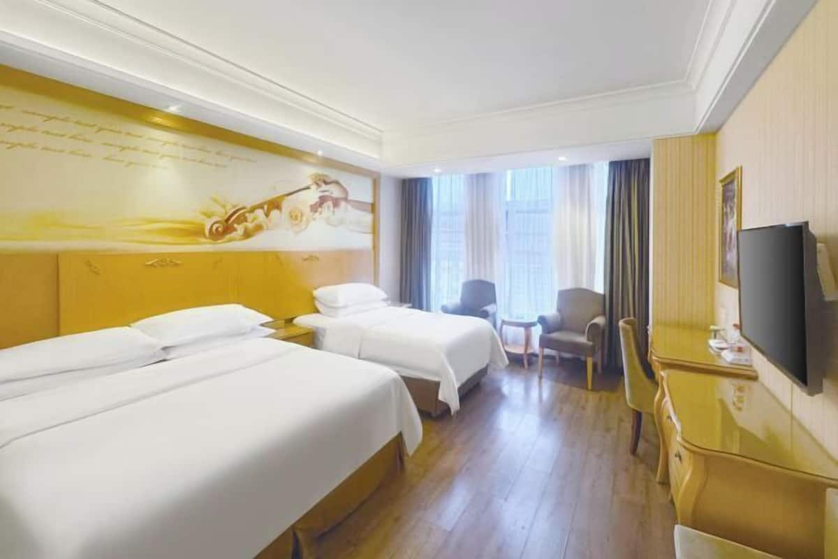A hotel room with two beds, a desk, a chair, a television, and a mural on the wall.