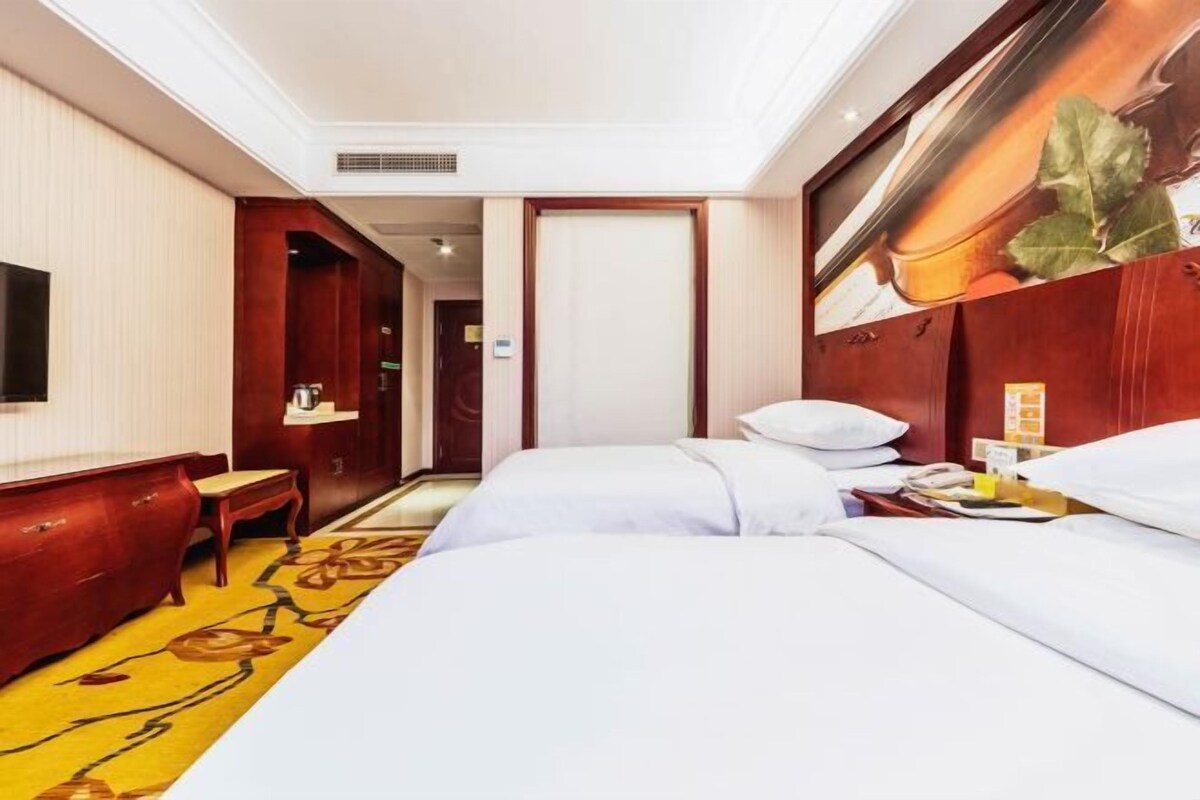 A hotel room with two beds, a TV, a desk, and a red wall.