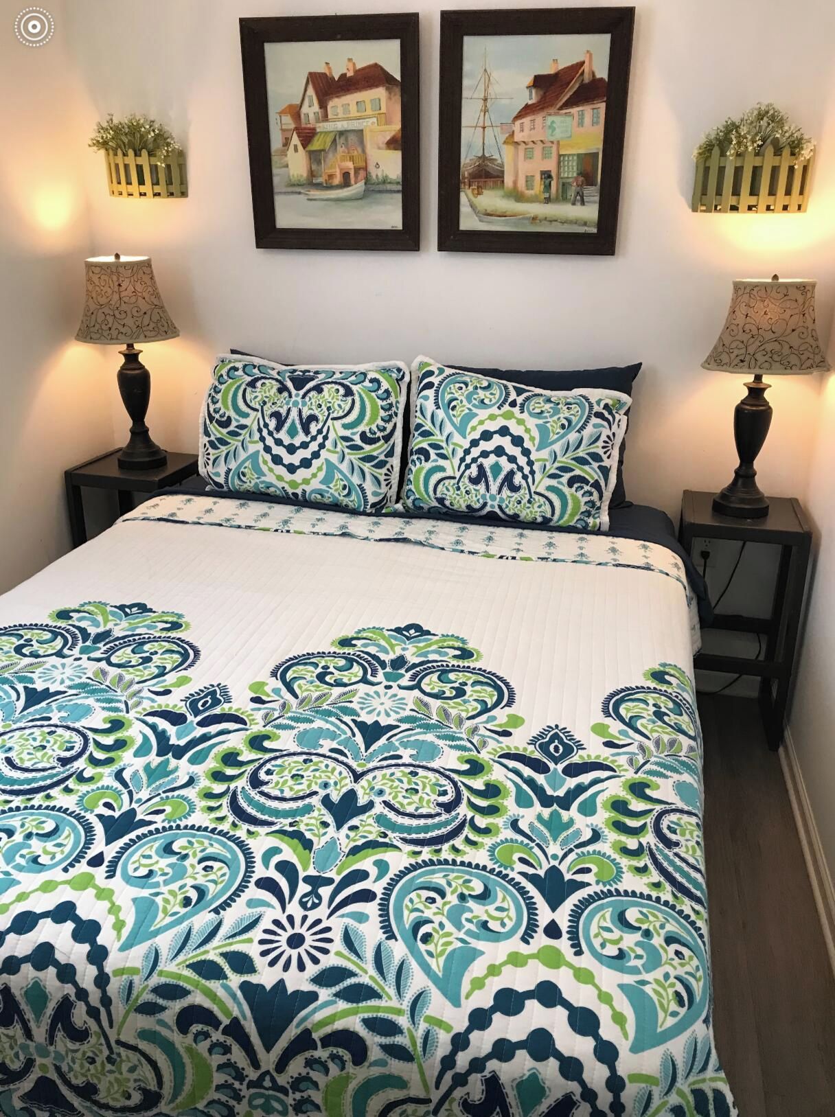 A bedroom with a bed, two nightstands, two lamps, and two framed pictures on the wall.
