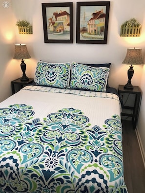 A bedroom with a bed, two nightstands, two lamps, and two framed pictures on the wall.