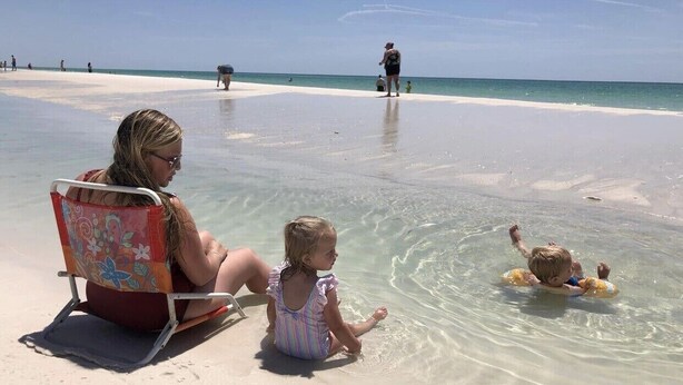 A beach scene with a woman and a child sitting on a beach chair, a child in the water, and another person in the background. - Bam!!! August Special rate 79 guests love this little paradise!  Private pool! (Gulf Breeze)