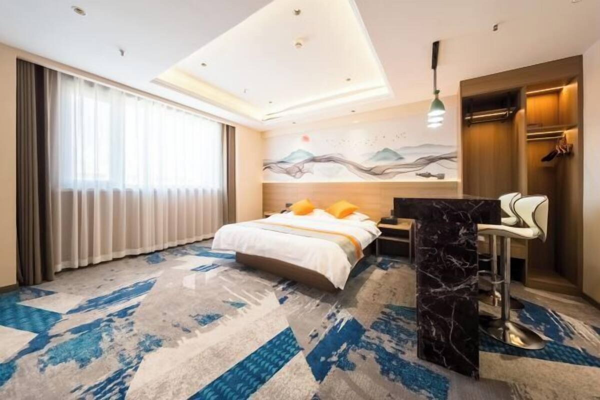 Habitación de hotel con cama, escritorio, silla, tocador y un gran ventanal.