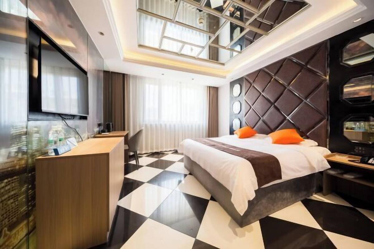Una habitación de hotel moderna con piso a cuadros, una cama con ropa de cama blanca y marrón, un escritorio con una computadora y un espejo grande en la pared.